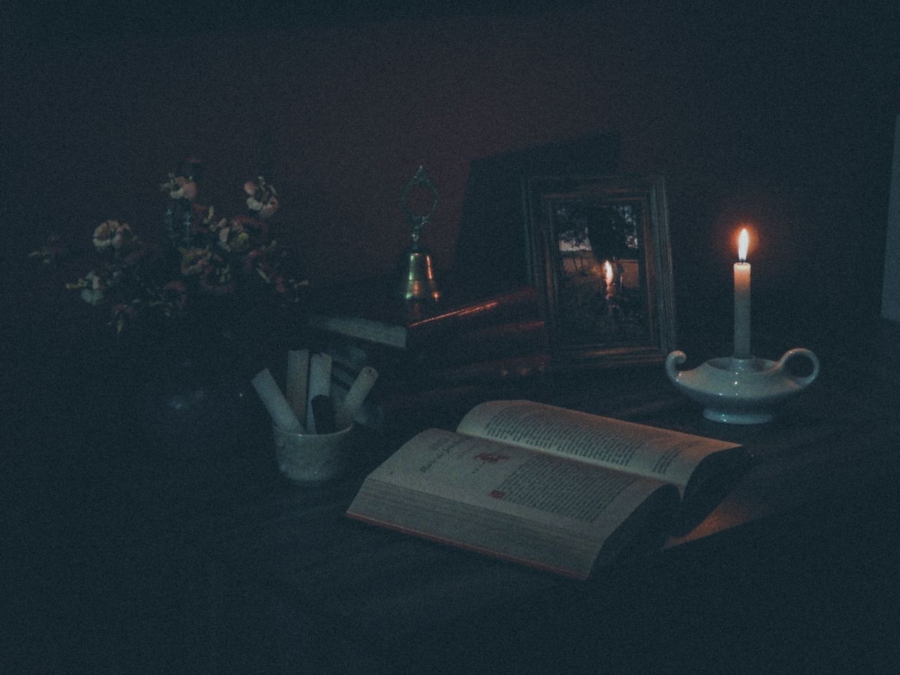 services-img-04 A dimly lit still life featuring an open book and a candle casting a warm glow.