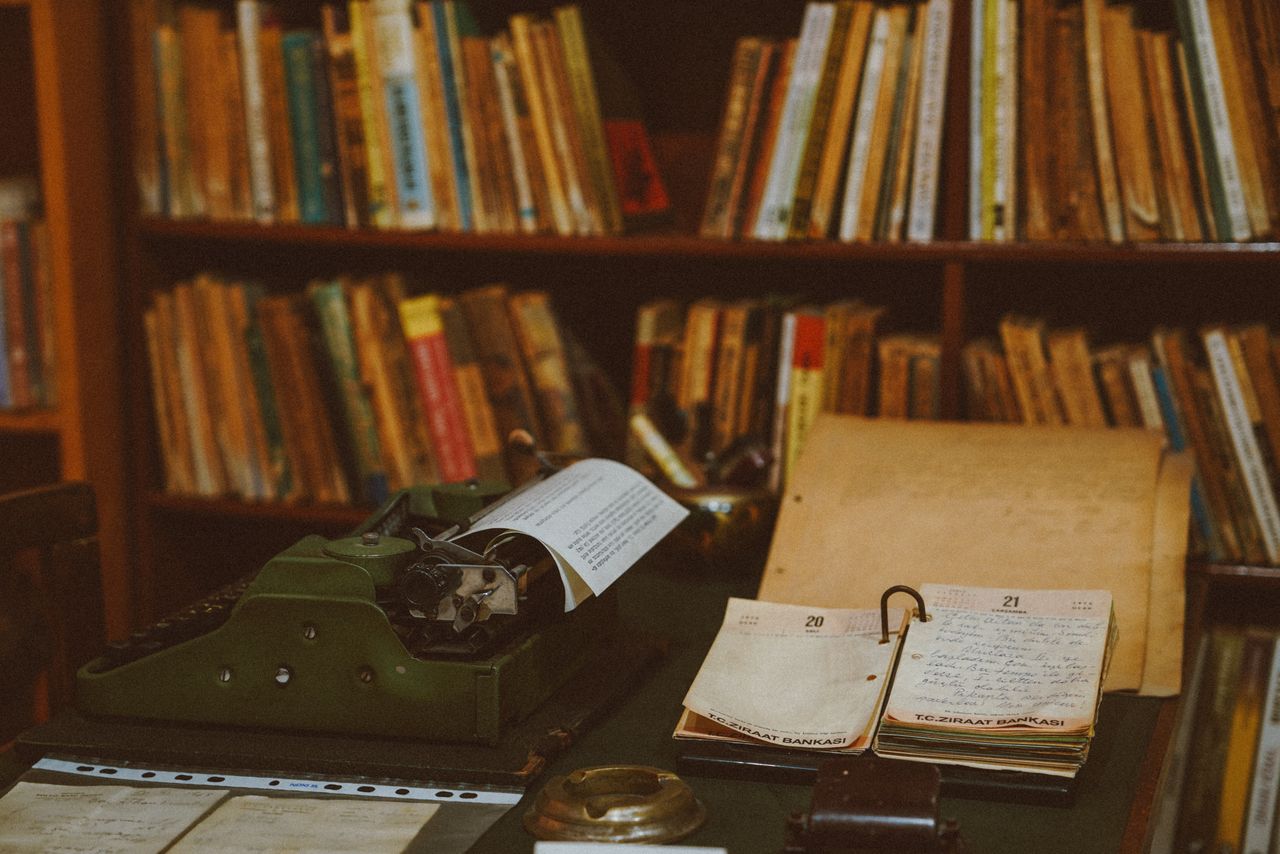 our-services-01 A vintage typewriter and notebooks sit on a desk in a cozy library filled with books.