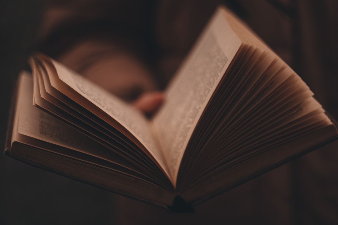 about-us-img Close-up of an open book with pages fanned out in moody lighting.